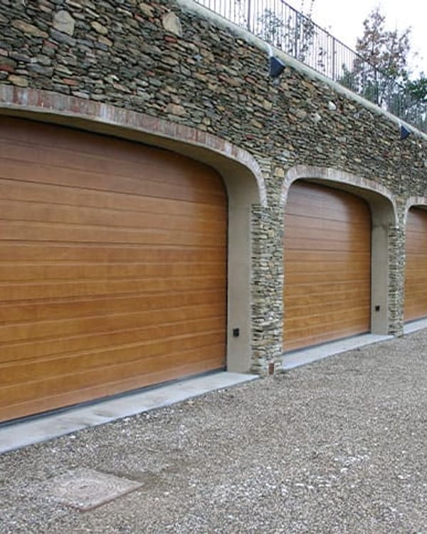 Portoni sezionali con finitura effetto legno sotto archi in pietra