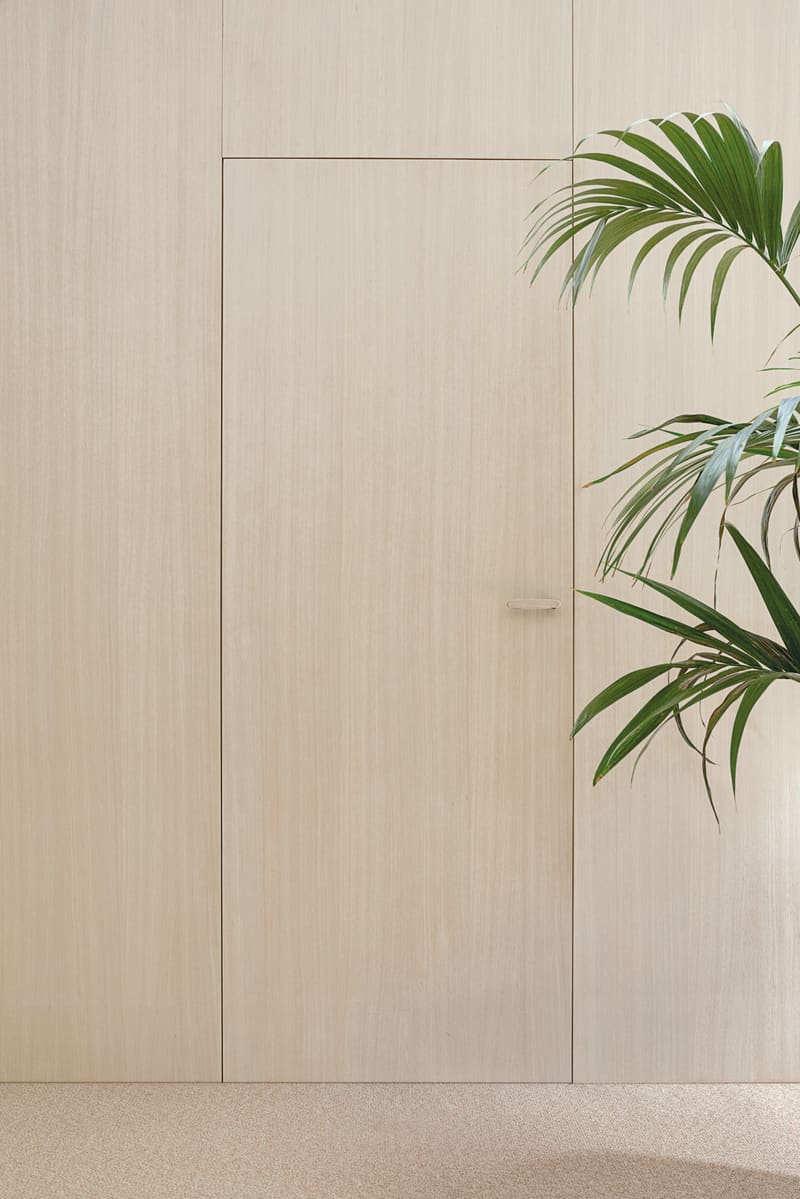 Porta filomuro in rovere chiaro integrata nella boiserie della parete, senza cornici a vista