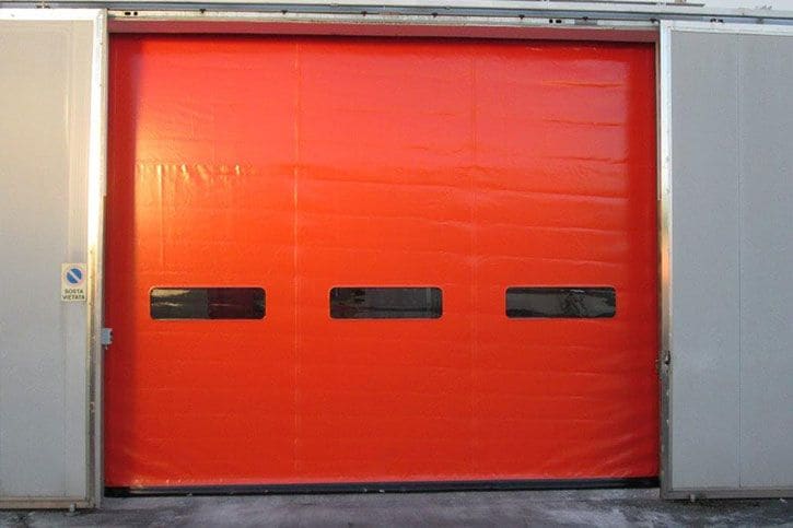 Porta rapida industriale a telo in PVC rosso con oblò su un capannone produttivo