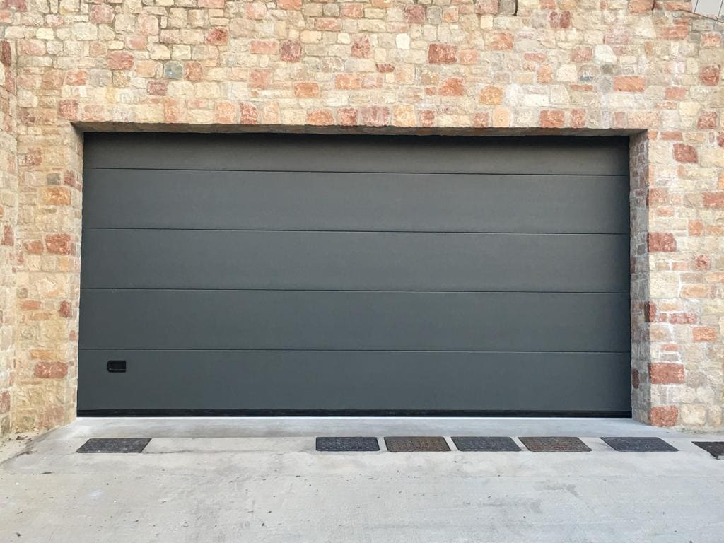 Portone sezionale grigio antracite a pannelli lisci installato su una facciata in pietra