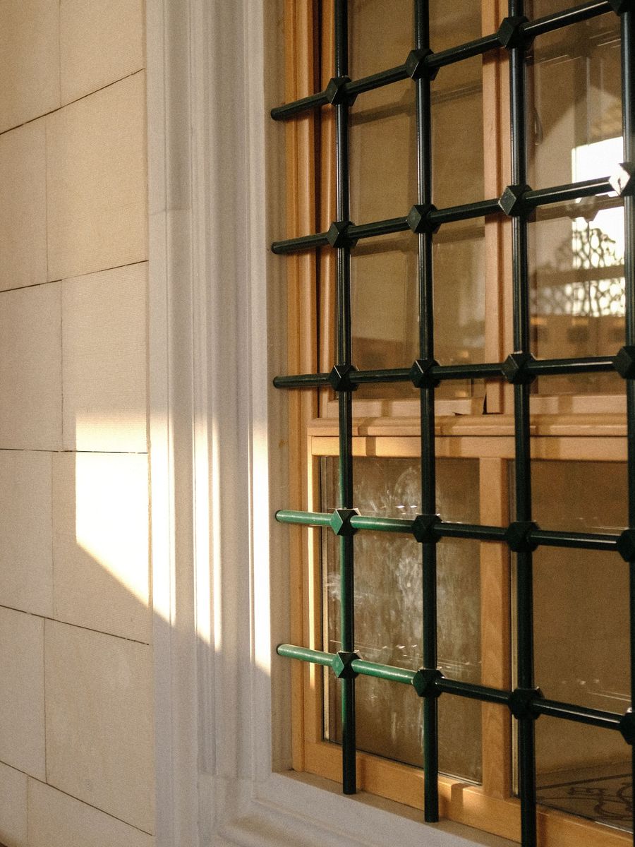Inferriata moderna a griglia su una finestra in legno, controluce con ombre nette sulla parete